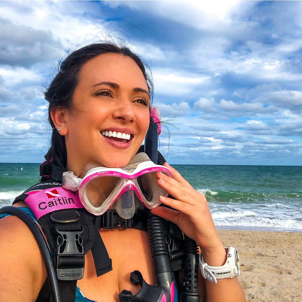 Female scuba diver on beach with personalized BCD name tag on right shoulder